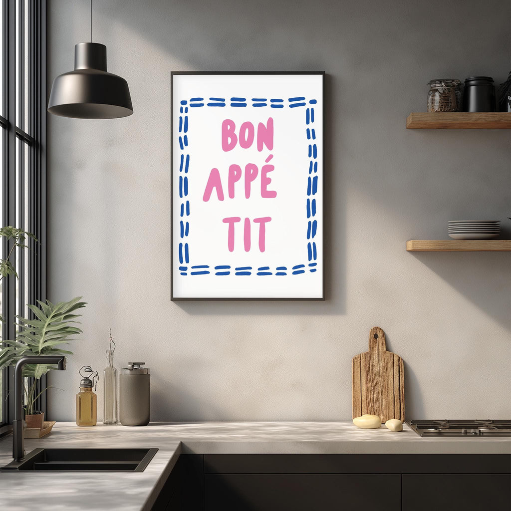 a kitchen counter with a framed poster hanging on the wall above it. The poster has the text " bon appe tit" written in pink and blue.