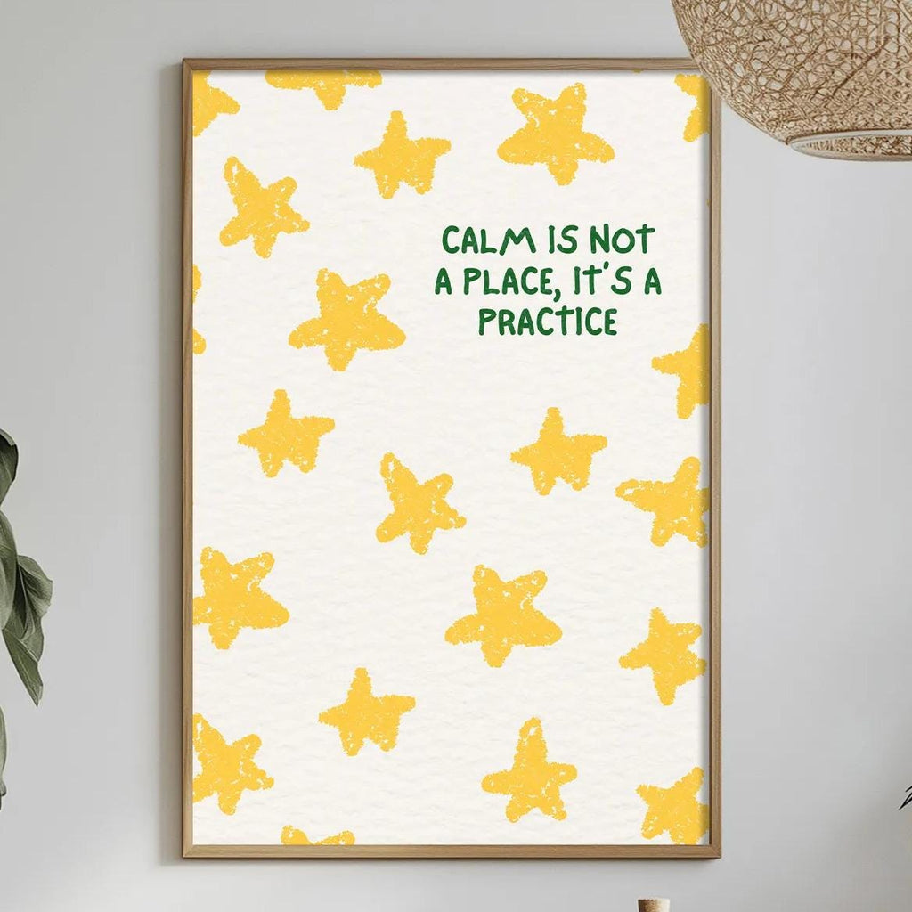 a dining table with a white tablecloth, a bowl of fruit, a bottle, and a vase with flowers. Above the table, there is a framed poster with a yellow star pattern and the text "Calm is not a place, it's a practice" displayed on it.
