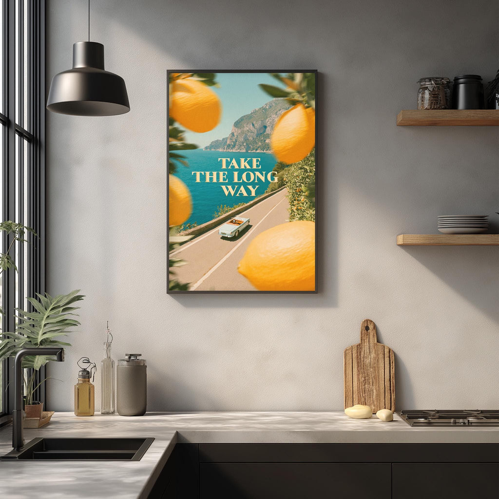 a kitchen counter with various kitchen items, such as a cutting board, a bottle, and a bowl, as well as a framed poster with the text "Take the long way" and an illustration of a road with orange lemons.