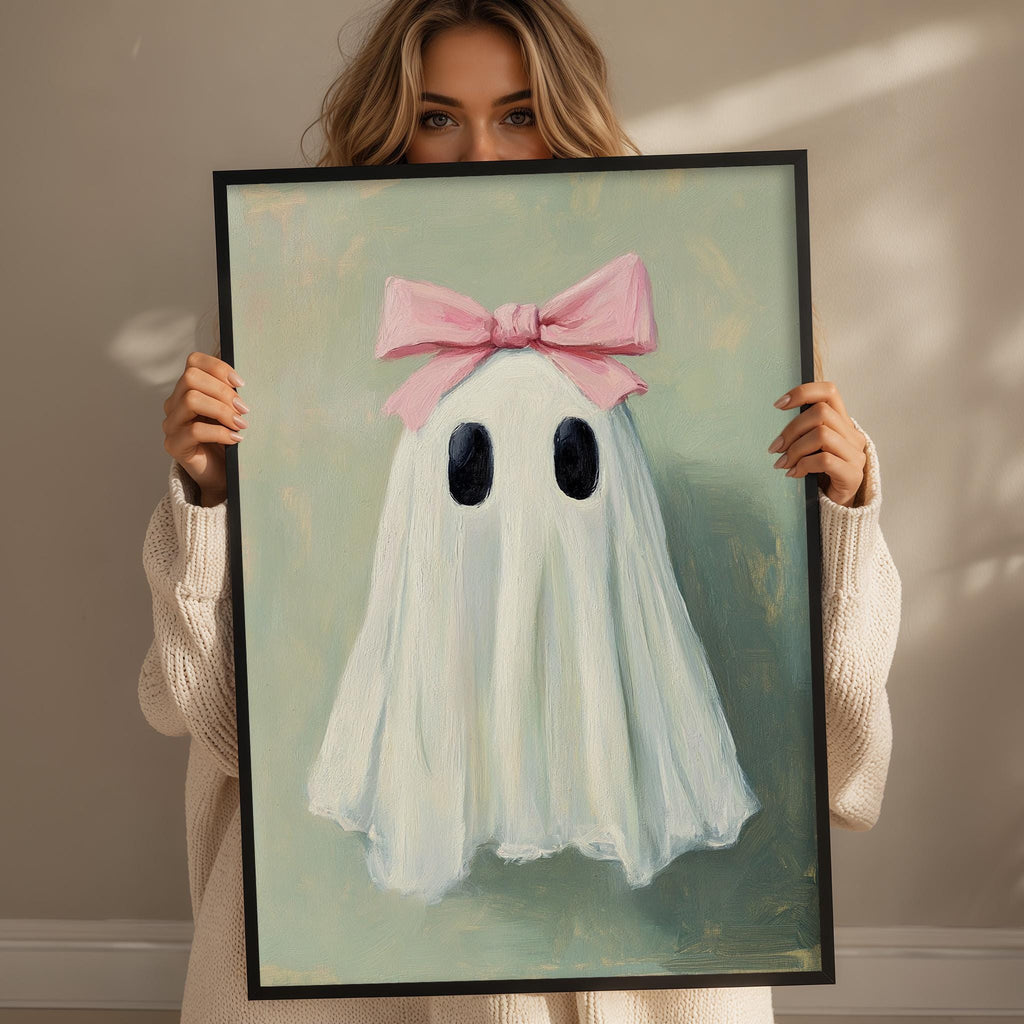 A woman holds a framed painting of a ghost with a pink bow on its head.