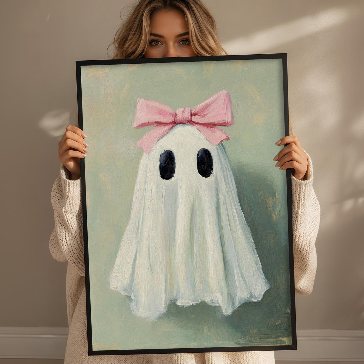 A woman holds a framed painting of a ghost with a pink bow on its head.