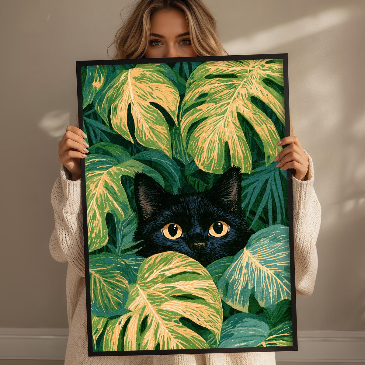A woman holds up a framed print of a black cat peeking out from a lush, tropical plant backdrop.