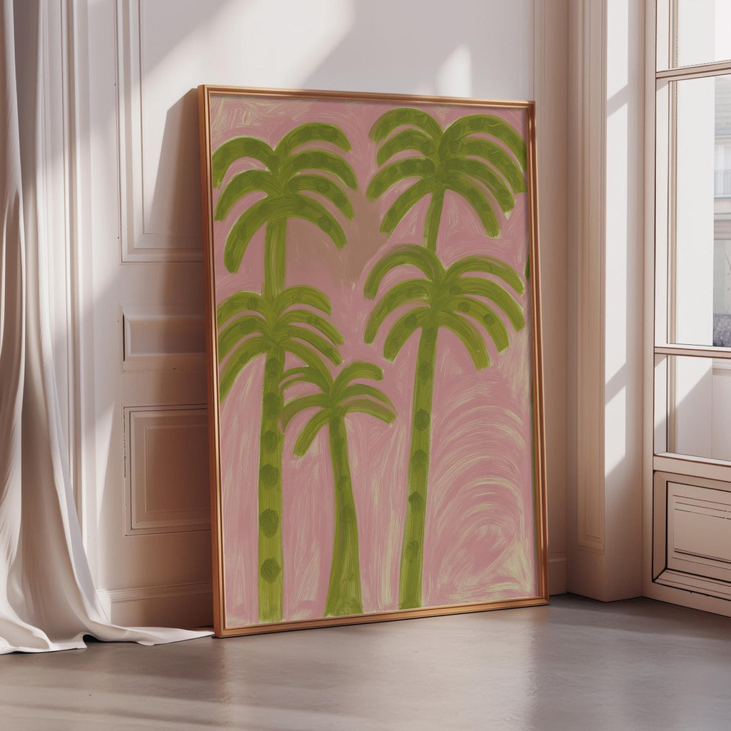 a large framed painting of palm trees in a pink background, placed on a wooden floor in a room with a window.