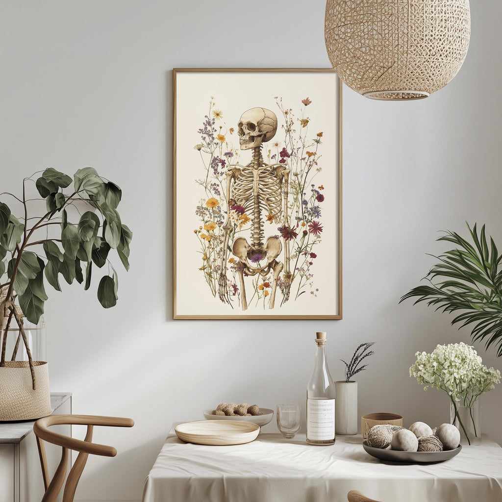 a dining table with a white tablecloth, a bowl of fruit, a bottle, and a vase with flowers. Above the table, there is a framed picture of a skeleton surrounded by flowers.