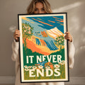 A woman holding a framed poster with a colorful illustration of a landscape and the text "IT NEVER ENDS"