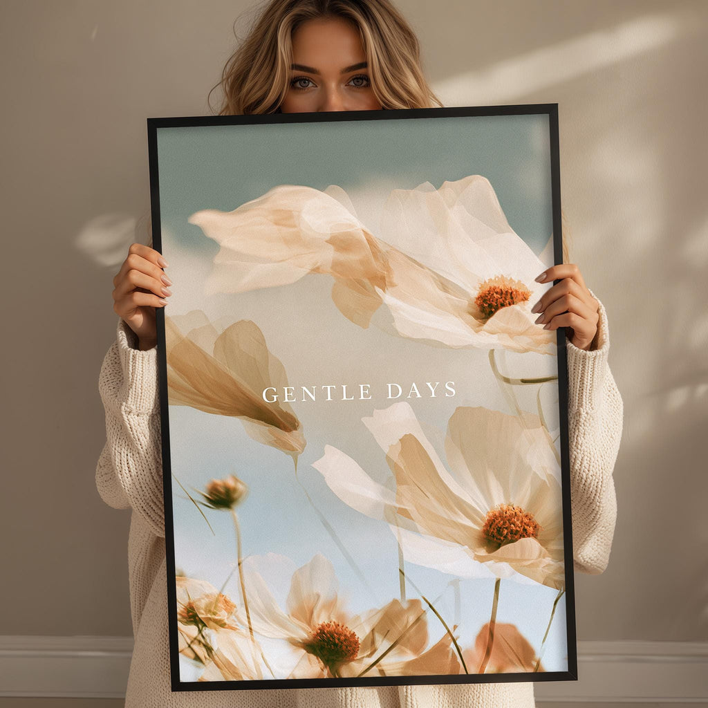 A woman holding a framed print with a floral design and the text "GENTLE DAYS" printed on it.