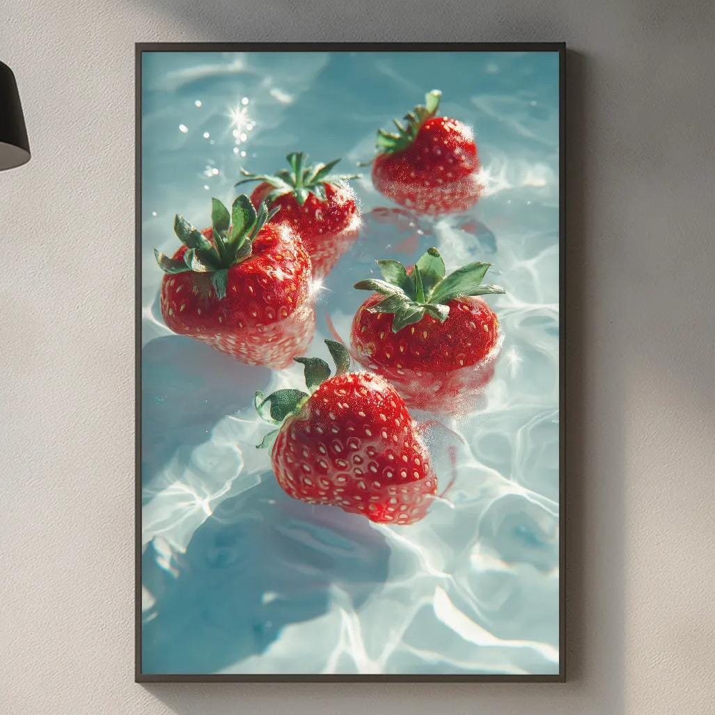 a framed photograph of red strawberries floating in a blue water surface, hanging on a wall above a kitchen counter.