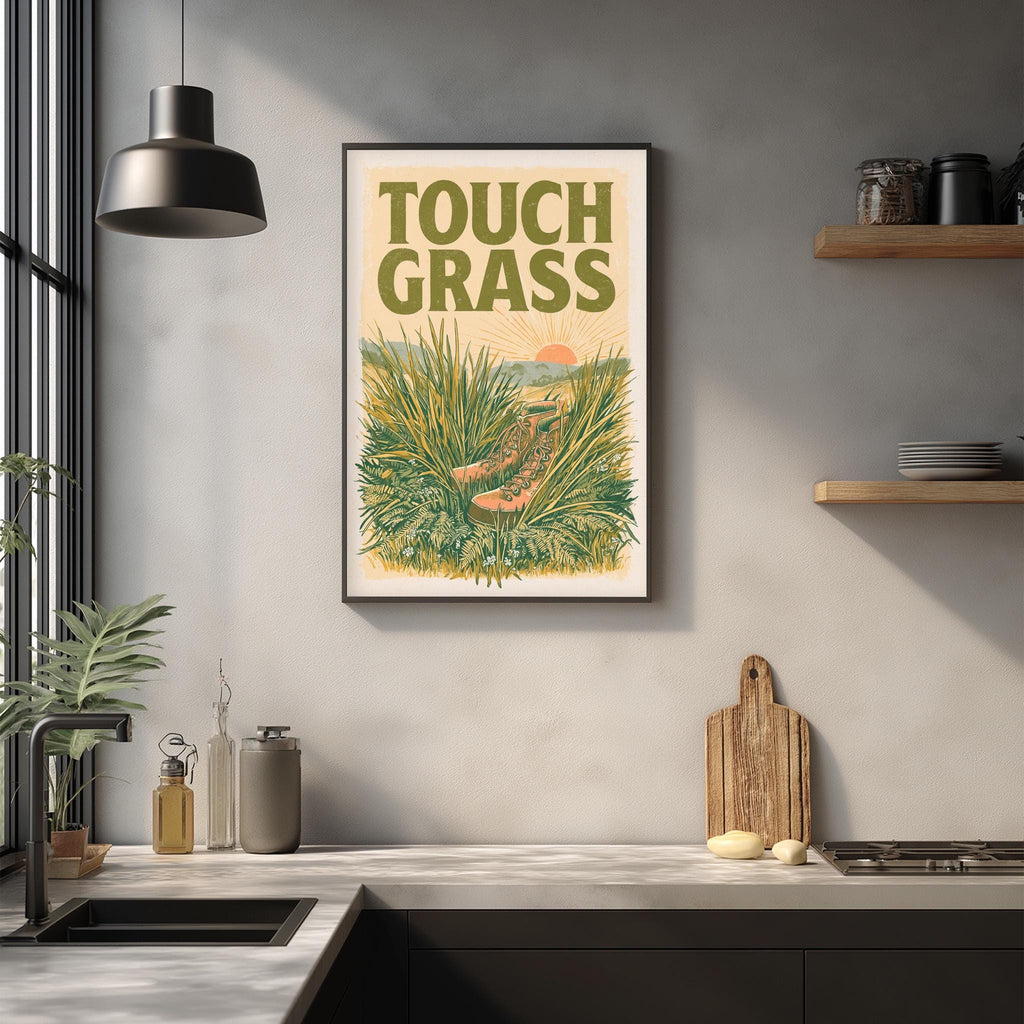 a framed poster of a lush green landscape with a sun-like figure in the center, hanging on a wall above a kitchen counter with various kitchen items and a wooden cutting board.
