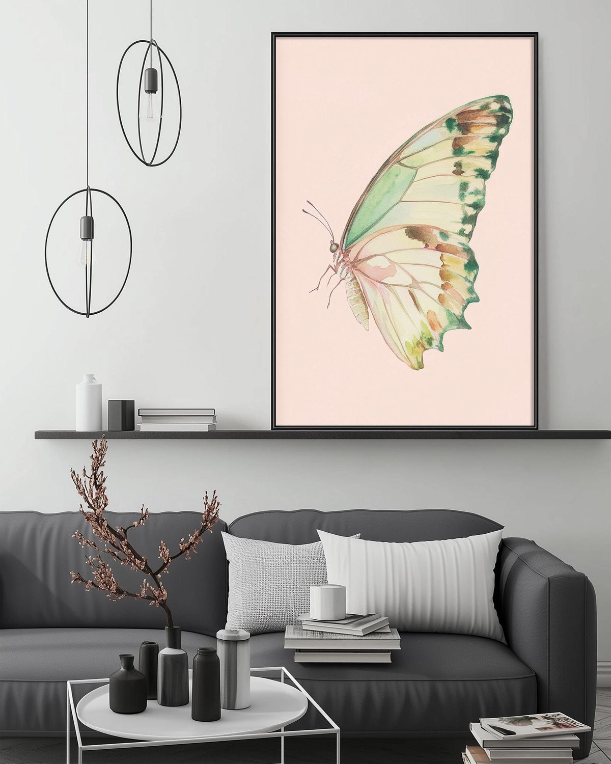 a large framed picture of a butterfly on a pink background, hanging on a wall above a gray couch with white pillows. The room has a minimalist and modern design, with a coffee table, pendant lights, and a shelf with decorative items.