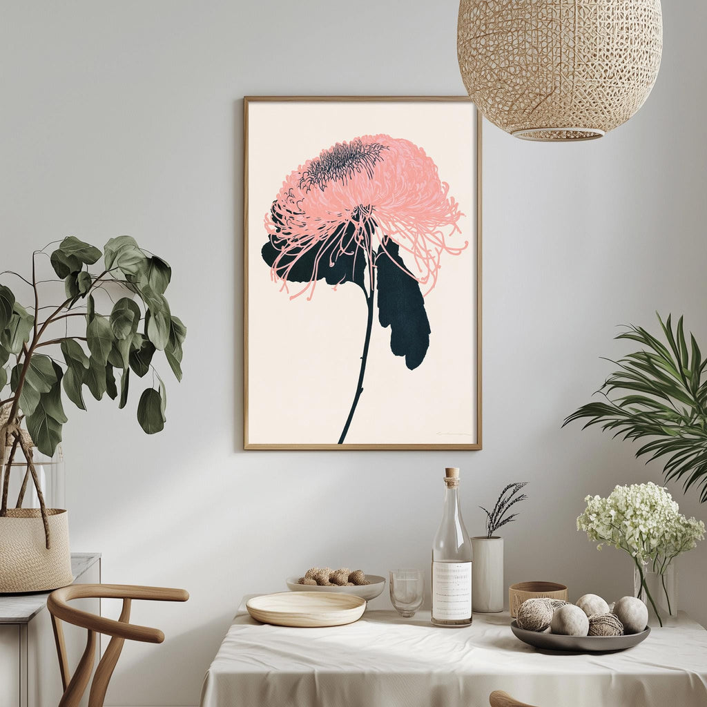 a dining table with a white tablecloth, a bowl of fruit, a bottle, and a vase with flowers. Above the table, there is a framed picture of a pink flower with black stems.