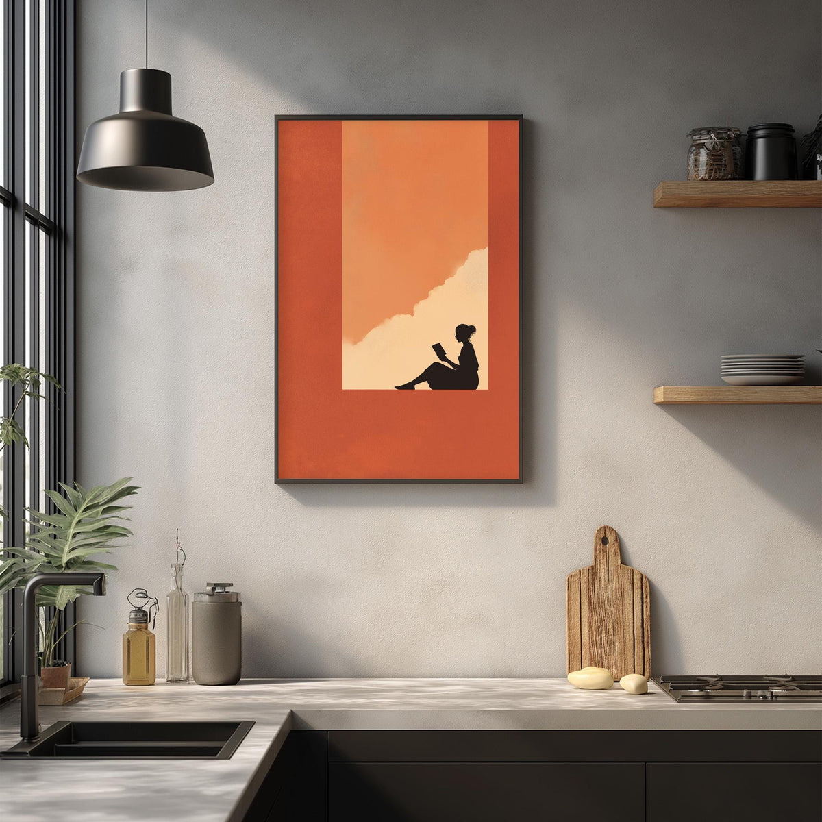a kitchen counter with various kitchen items, including a cutting board, a bottle, and a vase. Above the counter, there is a framed artwork depicting a silhouette of a person sitting and reading a book.
