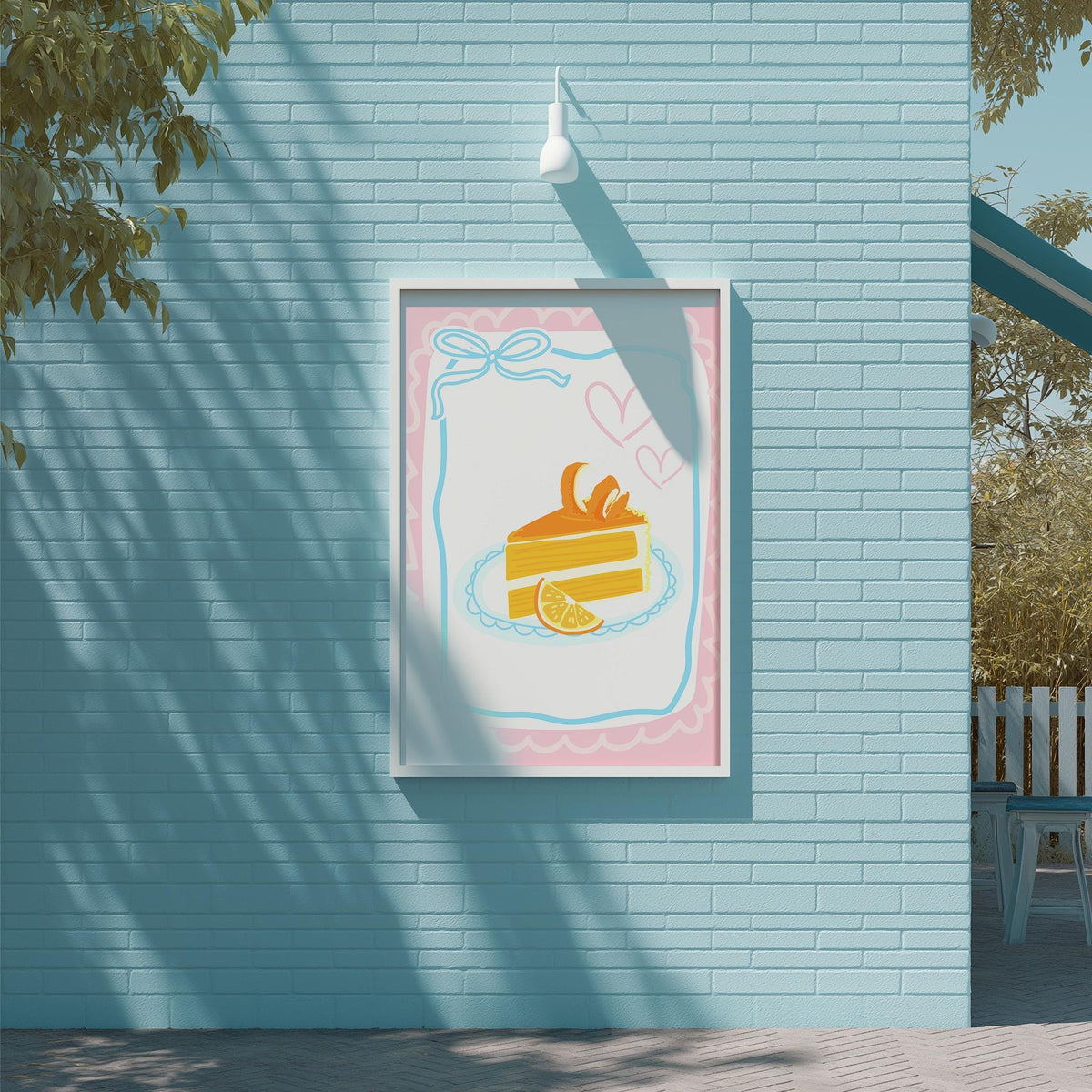 A framed illustration of a slice of cake with a heart and a slice of orange on a light blue brick wall.