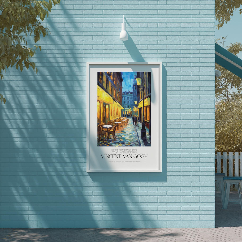 a framed painting of a street scene with a building and chairs, hanging on a blue wall.