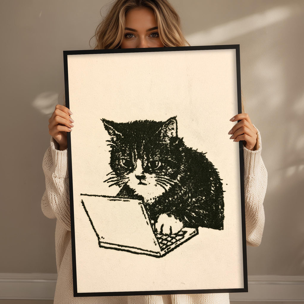 A woman is holding a framed print of a cat sitting on a laptop computer.