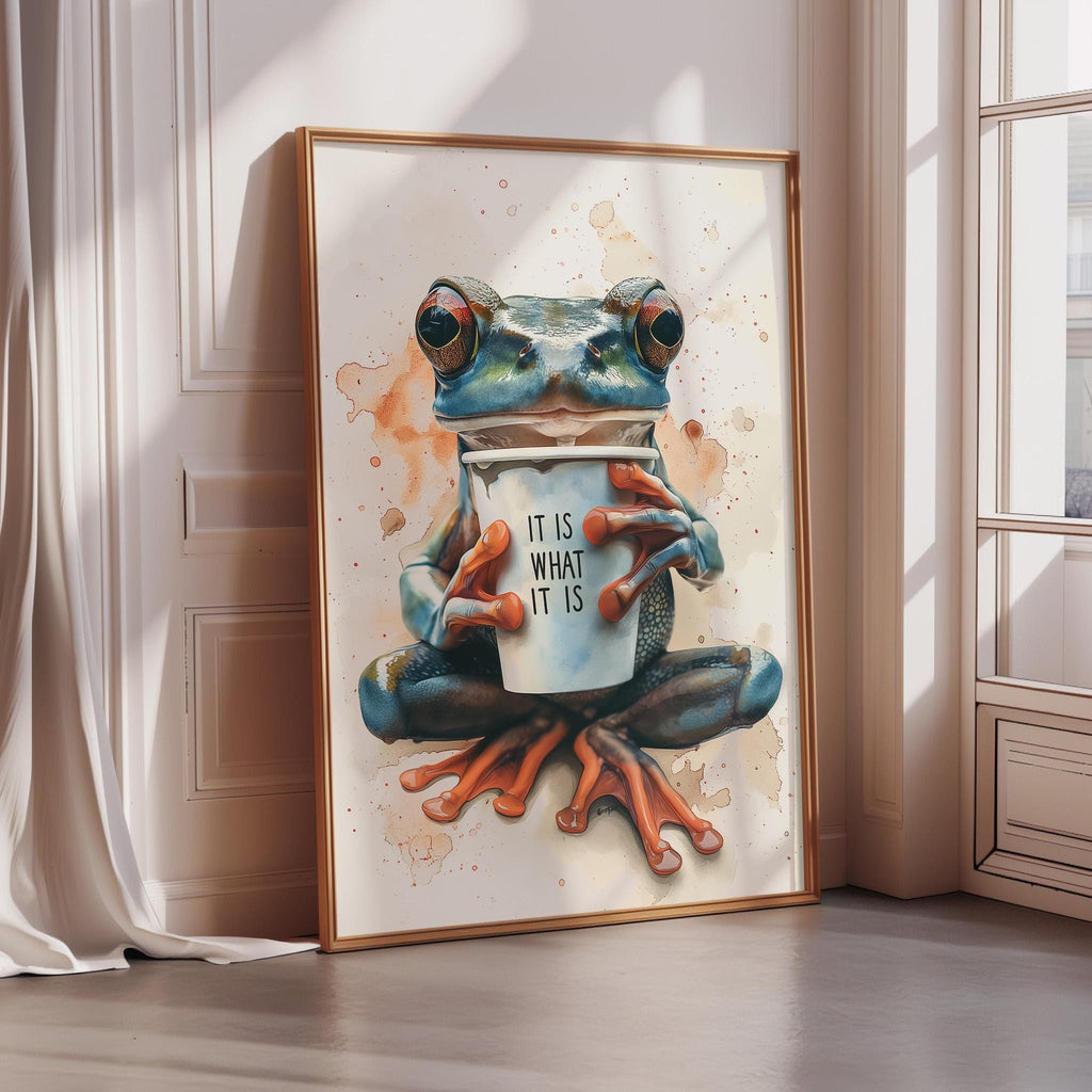 A framed painting depicting a blue frog sitting on a windowsill and holding a coffee cup with the text "IT IS WHAT IT IS" written on it.