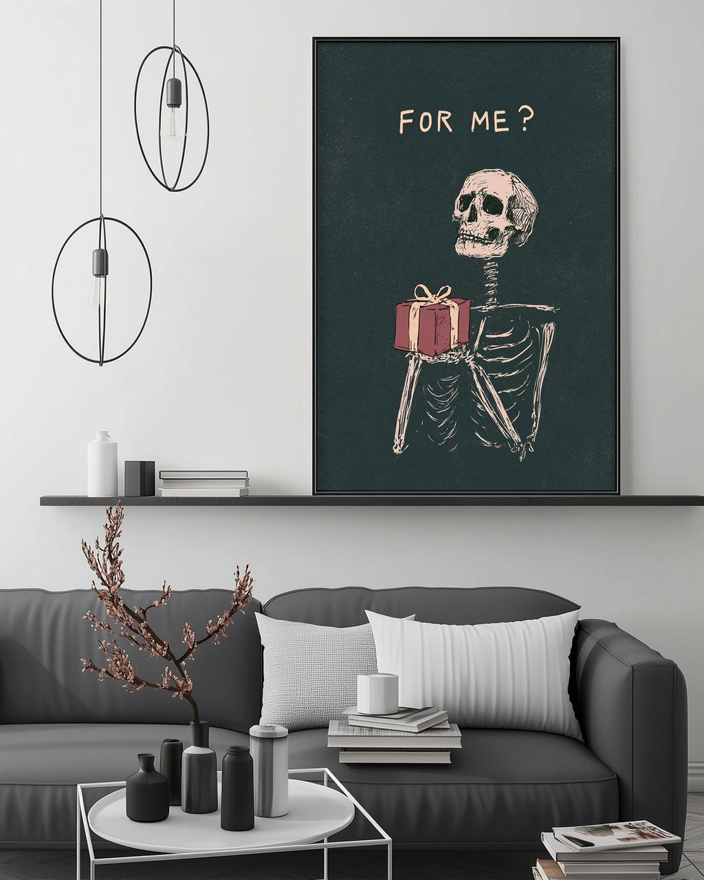 a living room with a gray sofa, a coffee table, and a large framed poster of a skeleton holding a gift. The poster has the text "FOR ME?" written on it.