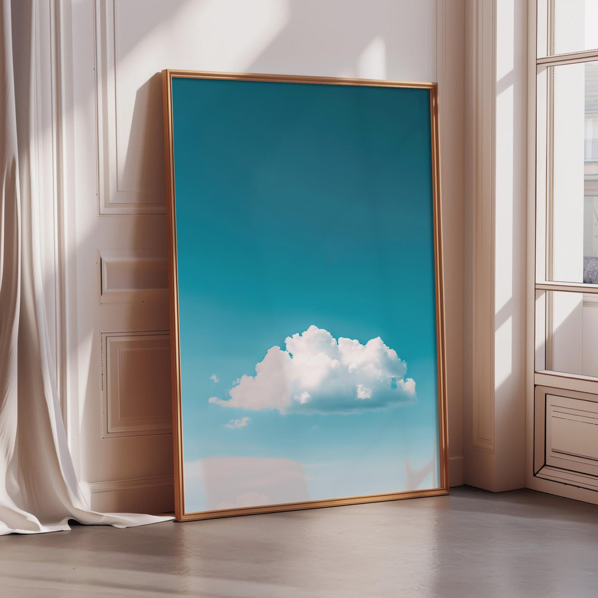 a large framed picture of a blue sky with a fluffy white cloud, placed on a wooden floor in a room with a window.