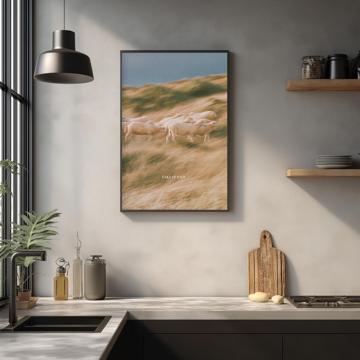 a framed photograph of a pastoral scene with a group of sheep grazing in a field, hanging on a wall above a kitchen counter with various kitchen items and decor.