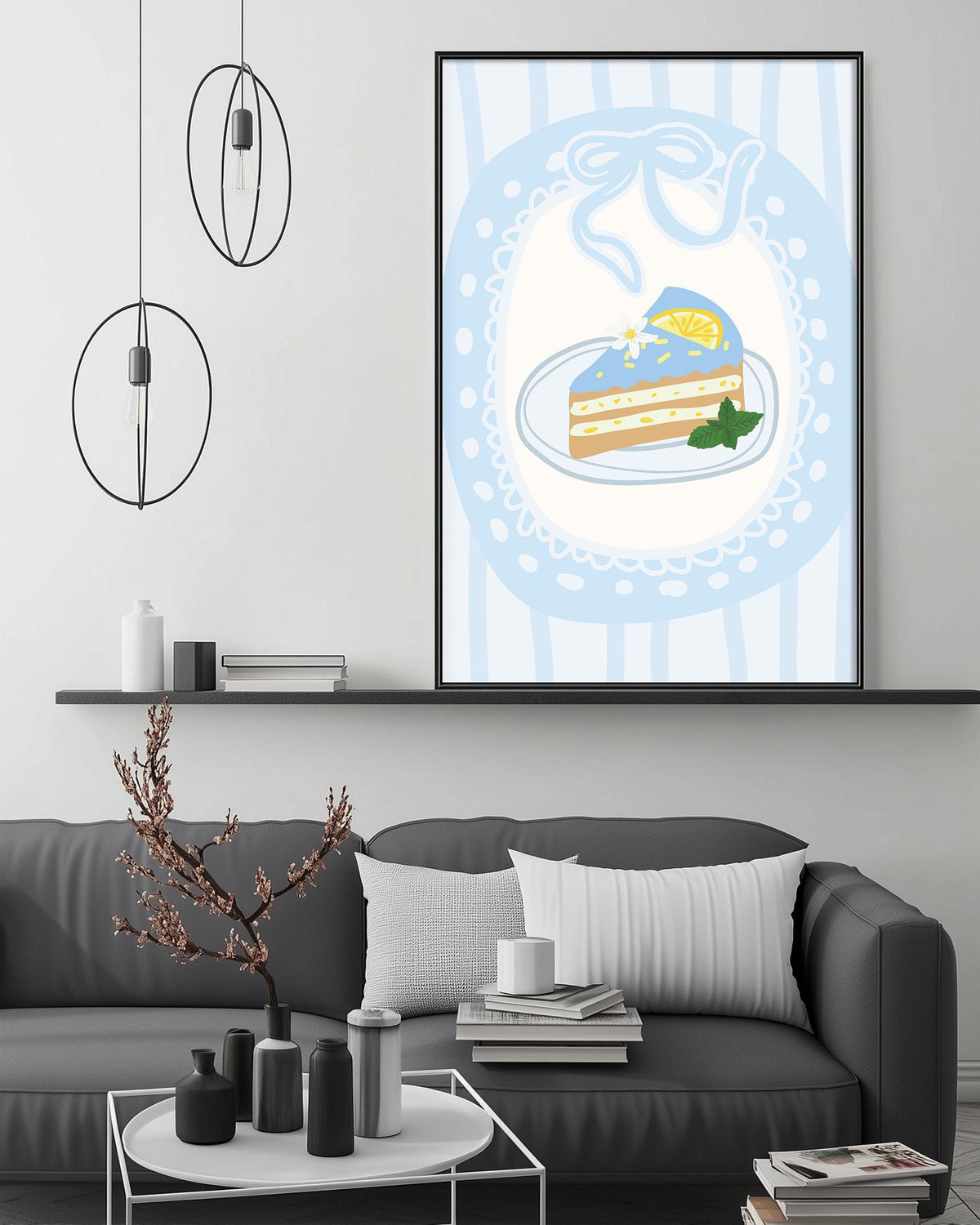 a cozy living room with a gray sofa, a coffee table, and a framed illustration of a slice of cake on a plate. The room has a minimalist and modern design, with pendant lights hanging above the sofa and a bookshelf filled with books.
