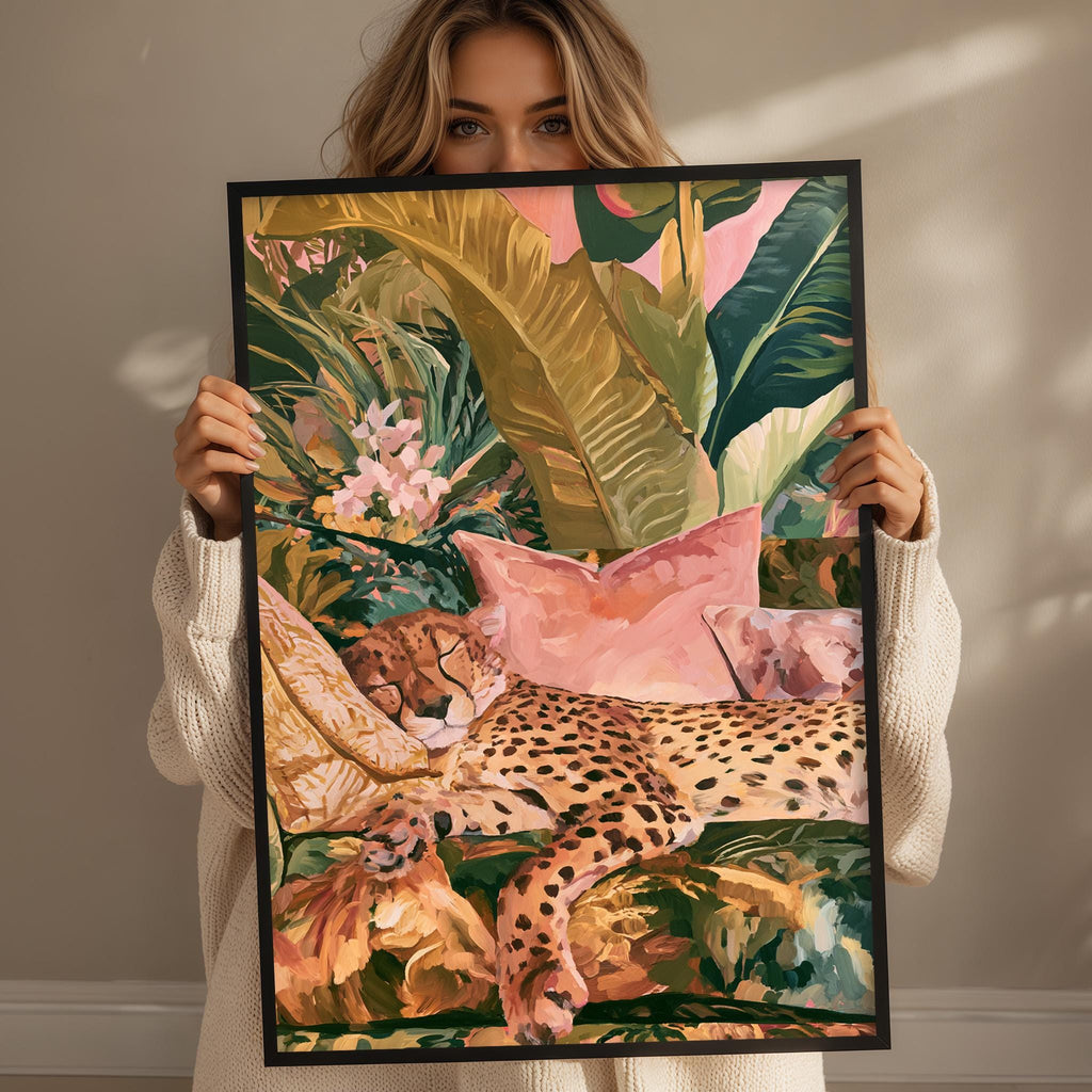 A woman holds up a framed painting depicting a leopard resting on a bed of flowers and leaves.