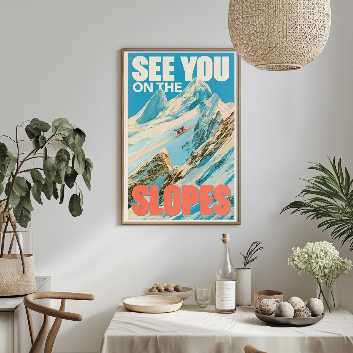 a framed poster of a mountain landscape with the text "See You on the Slopes" hanging on a wall above a dining table with various items on it.