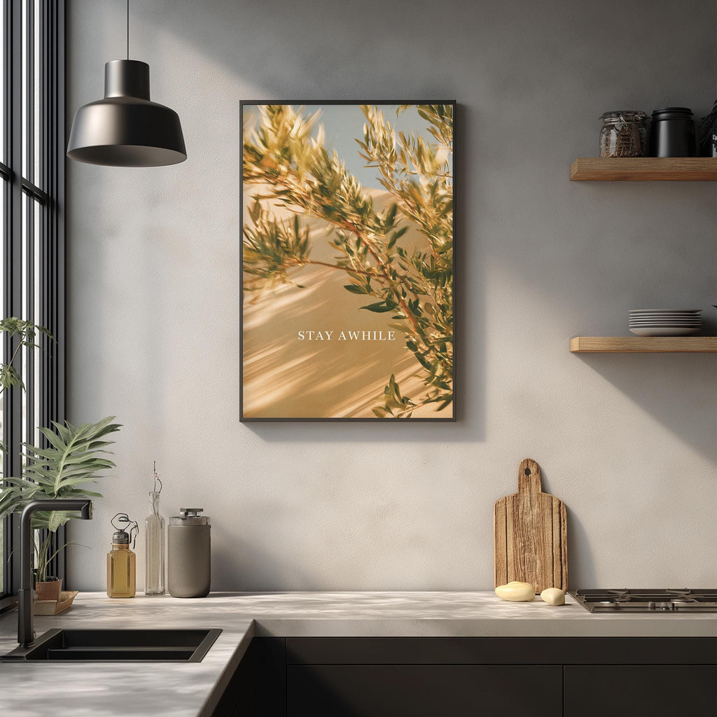 a kitchen counter with a framed picture of a plant, a wooden cutting board, and various kitchen items such as a bottle, a cup, and a bowl.