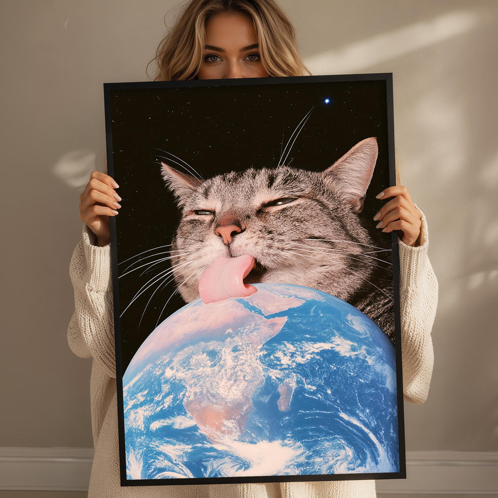 A woman holds up a framed image depicting a cat licking the Earth, with the planet visible in the background.