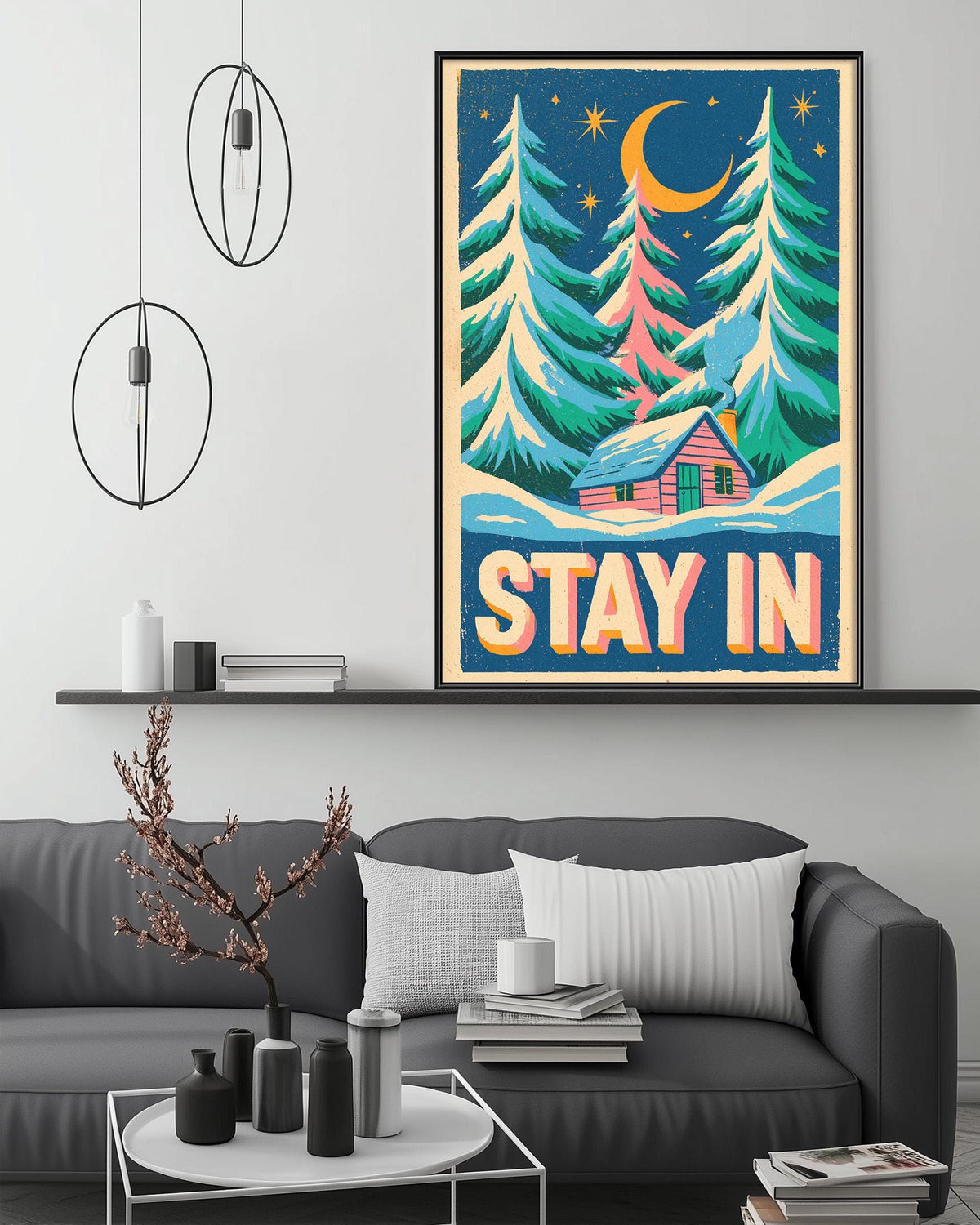 a cozy living room with a gray couch, a coffee table, and a framed poster of a snowy forest scene with a cabin. The poster has the text "STAY IN" written on it.
