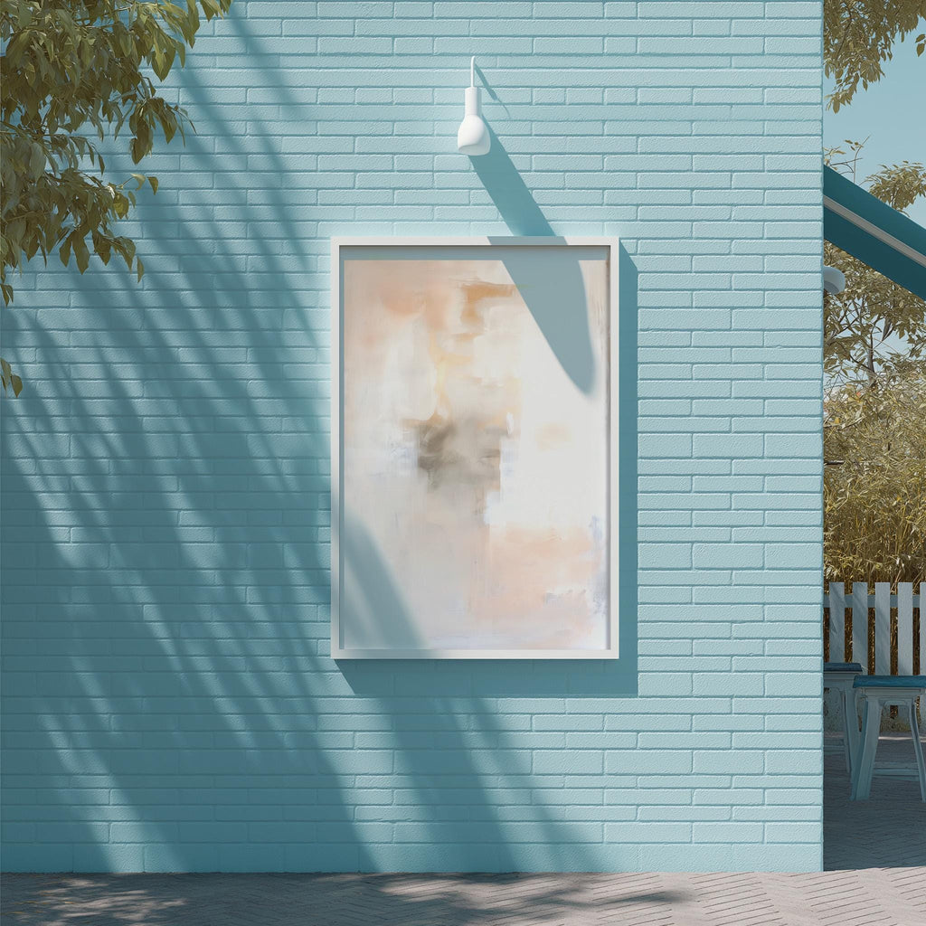 a blue brick wall with a framed abstract painting hanging on it. The painting has a white frame and a light fixture above it. The wall is situated next to a tree, and there is a bench visible in the background.