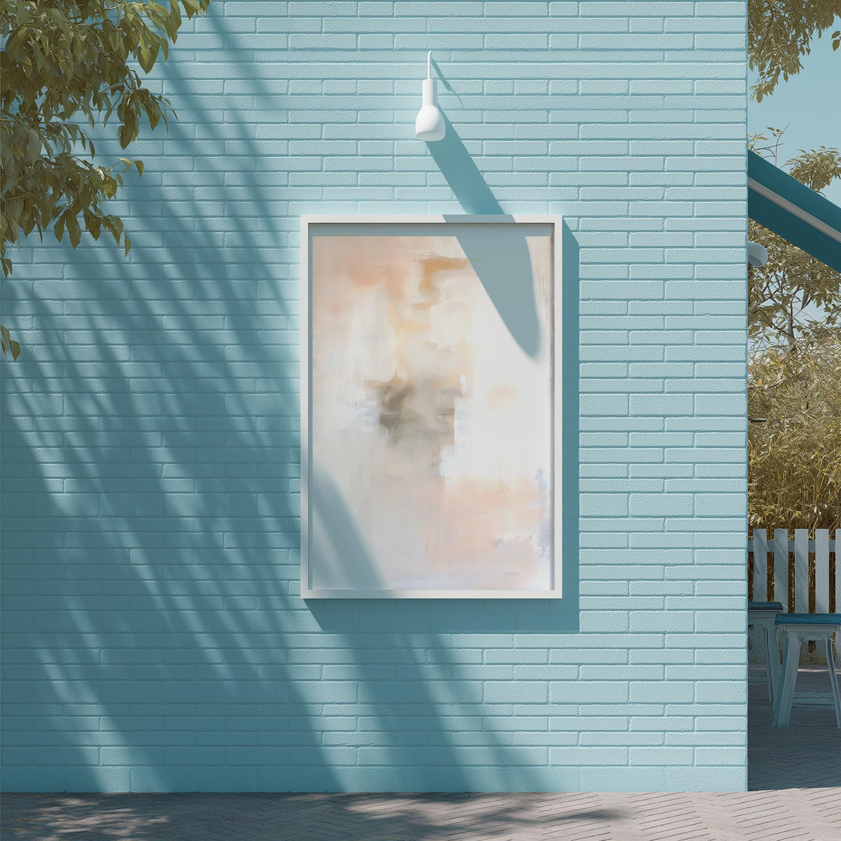 a blue brick wall with a framed abstract painting hanging on it. The painting has a white frame and a light fixture above it. The wall is situated next to a tree, and there is a bench visible in the background.