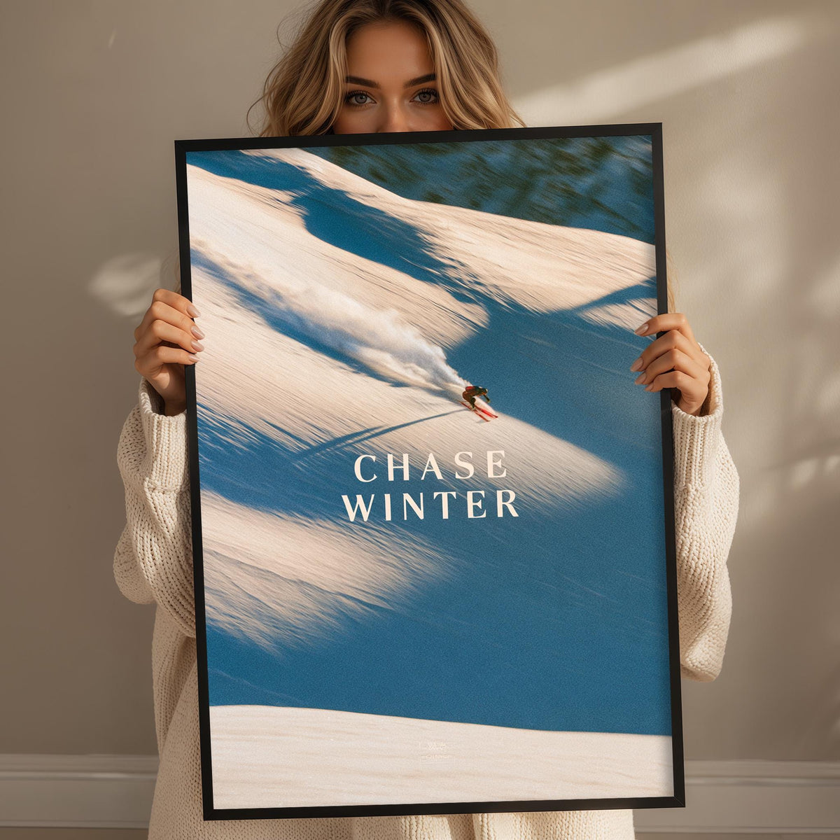 A woman holding a framed poster with a snowboarder on it, posing in front of a snowy mountain landscape.