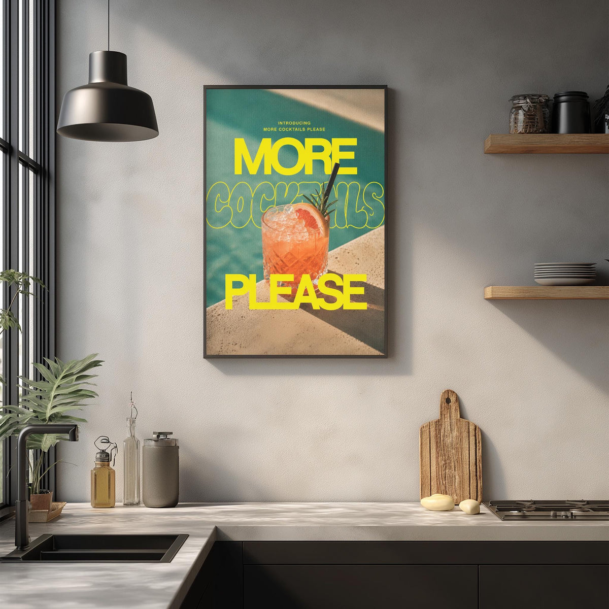 a framed poster with the text "MORE COCKTAILS PLEASE" hanging on a wall above a kitchen counter with various kitchen items such as a cutting board, a bottle, and a bowl.
