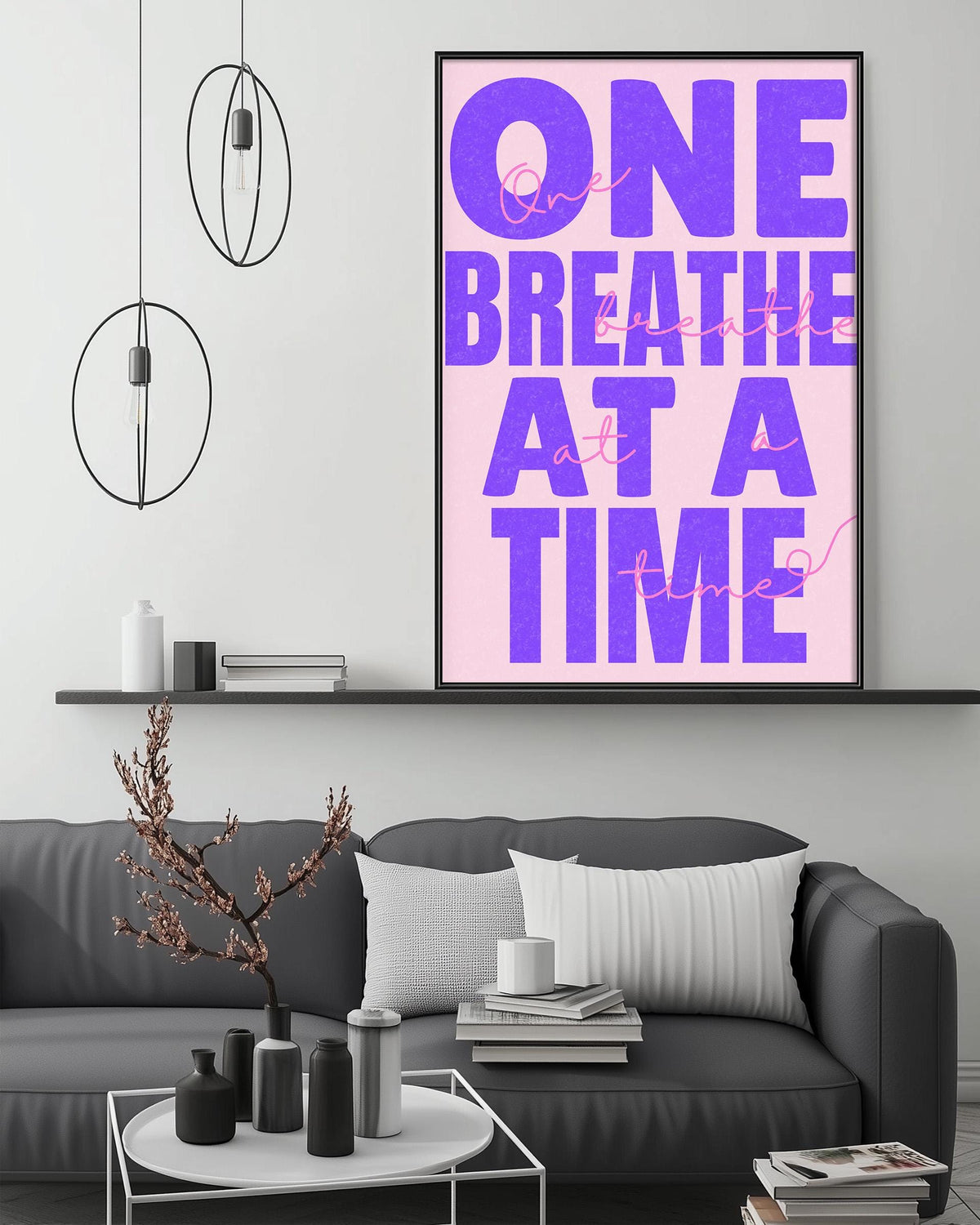 a modern living room with a gray sofa, a coffee table, and a large framed poster with the text "One breathe at a time" in purple and pink colors.