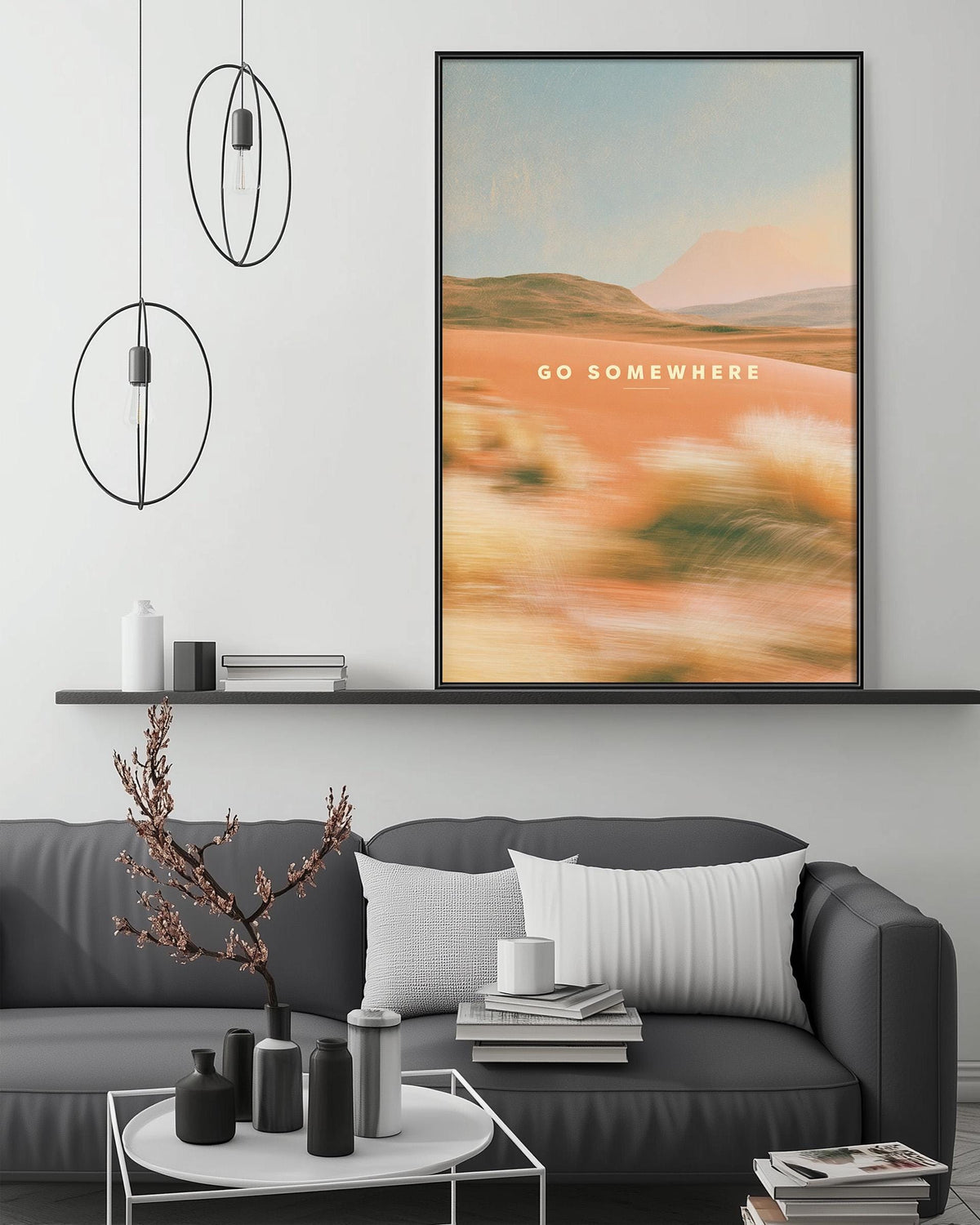 a modern living room with a gray sofa, a coffee table, and a large framed poster of a landscape with a quote that says "Go somewhere".