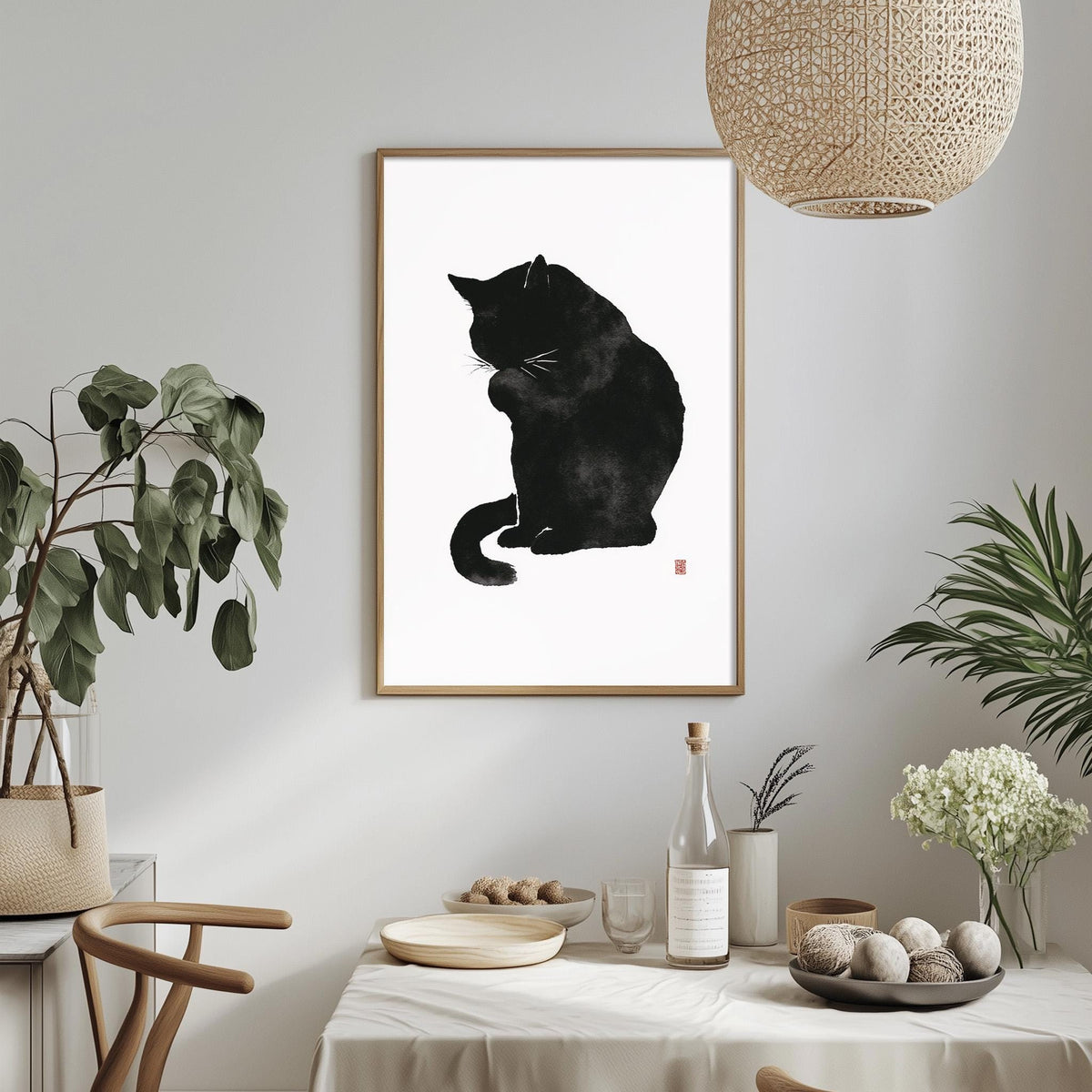 a black cat sitting on a white surface, with a framed picture of the cat hanging on the wall above a table with various items on it.