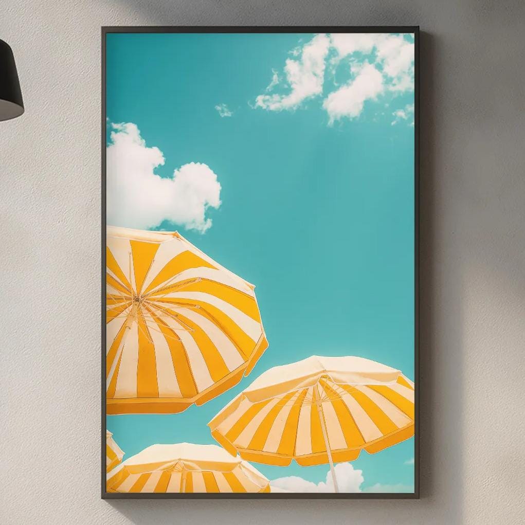 a kitchen counter with a framed picture of three orange and white striped umbrellas against a blue sky with white clouds.