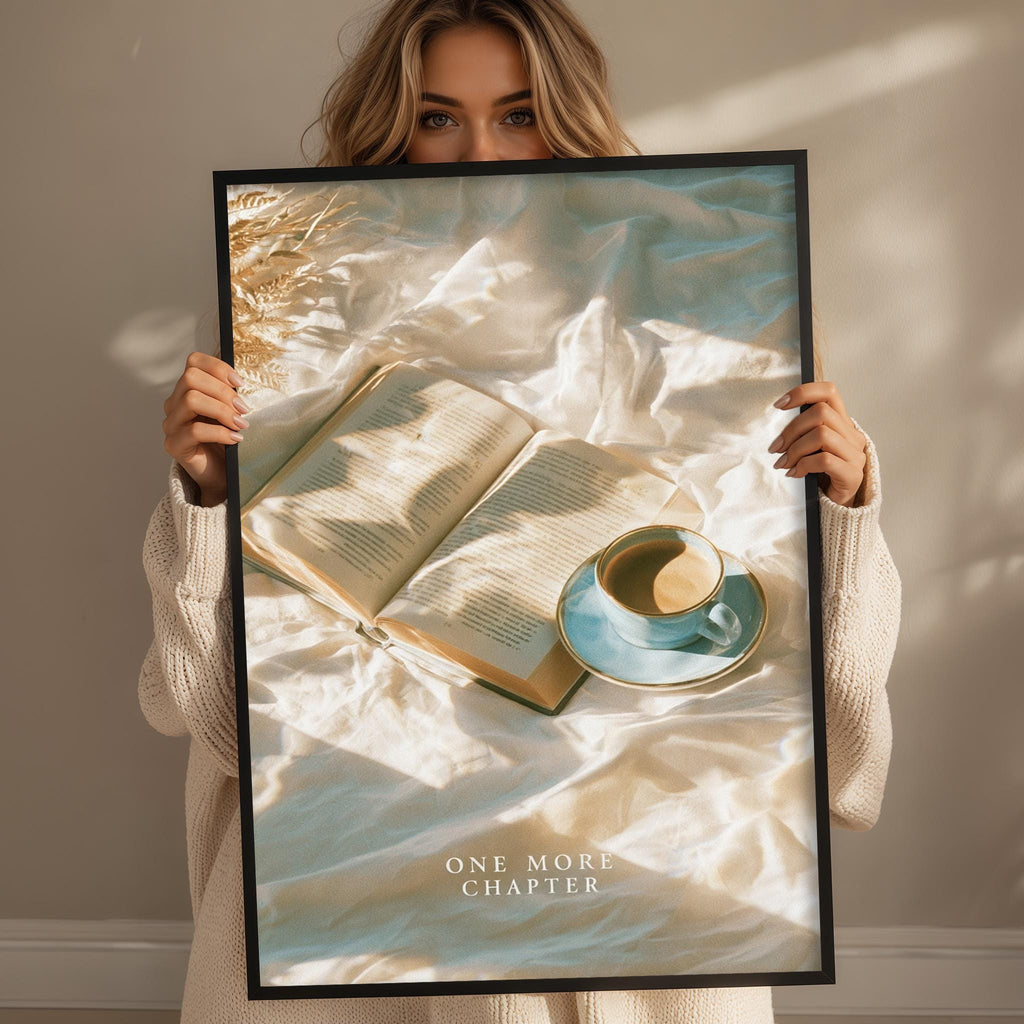 A woman holding a framed poster with an open book and a cup of coffee on a bed, with the text "ONE MORE CHAPTER" below the image.