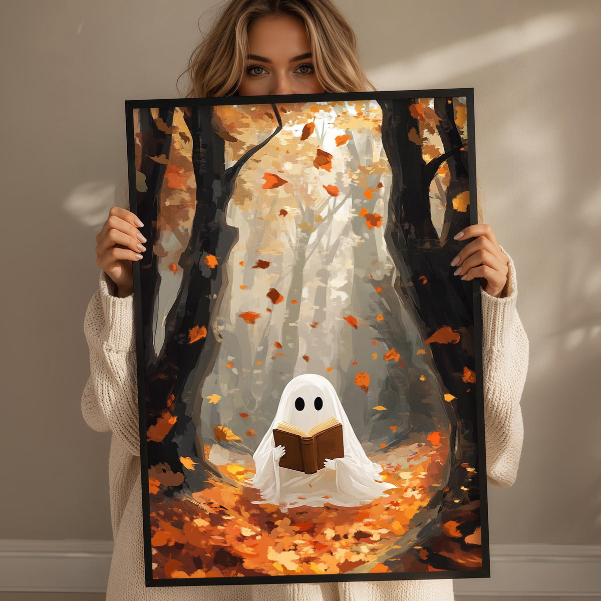 A woman holds up a framed artwork depicting a ghost reading a book in a forest with falling leaves.