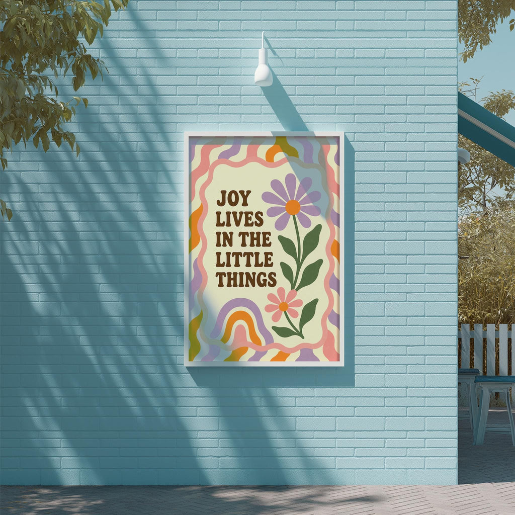 a poster with a colorful design and the text "Joy lives in the little things" displayed on a blue brick wall.