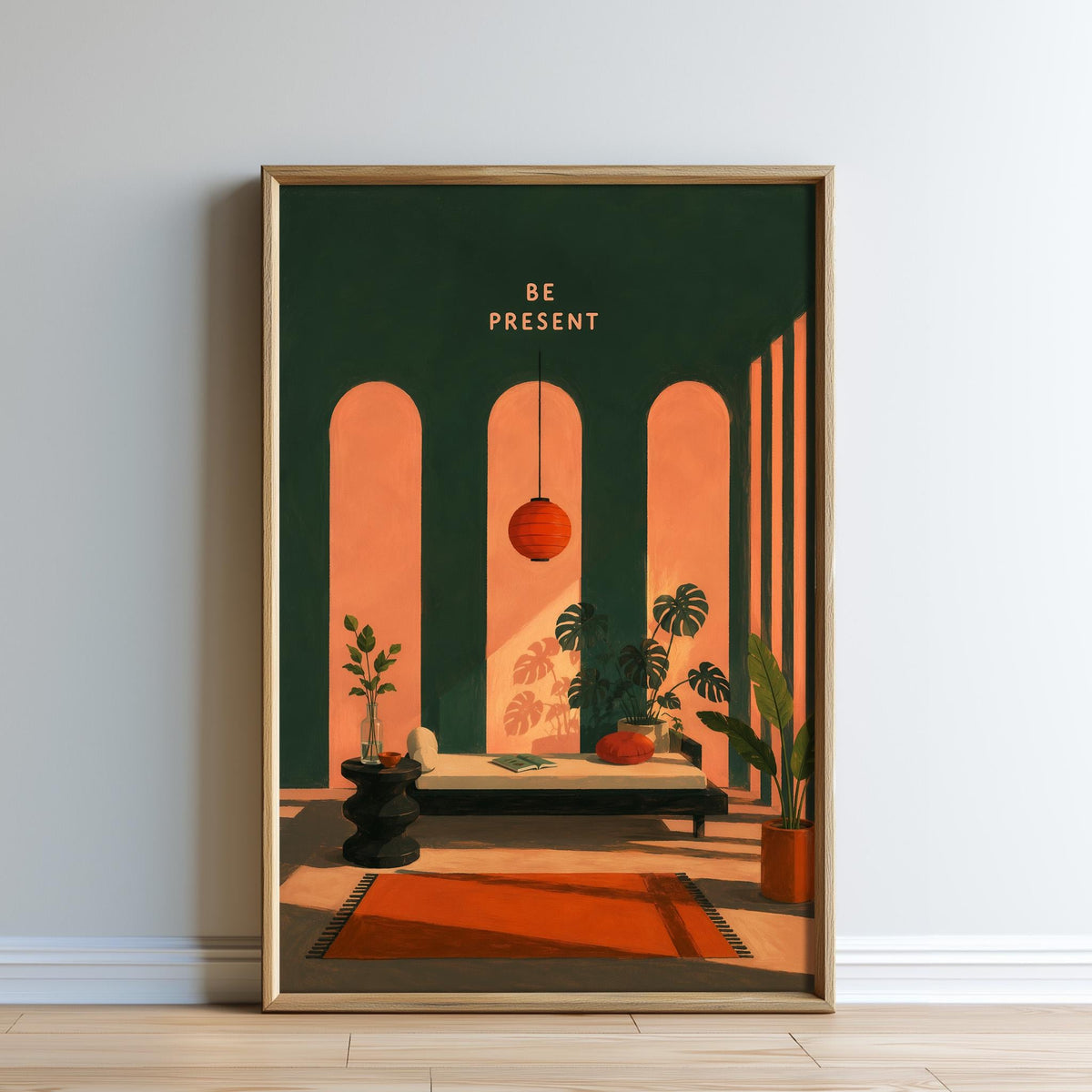 The image is a framed poster with a minimalist design featuring a green wall, a red rug, a black stool, a red lamp, and a plant. The text "BE PRESENT" is displayed above the poster.
