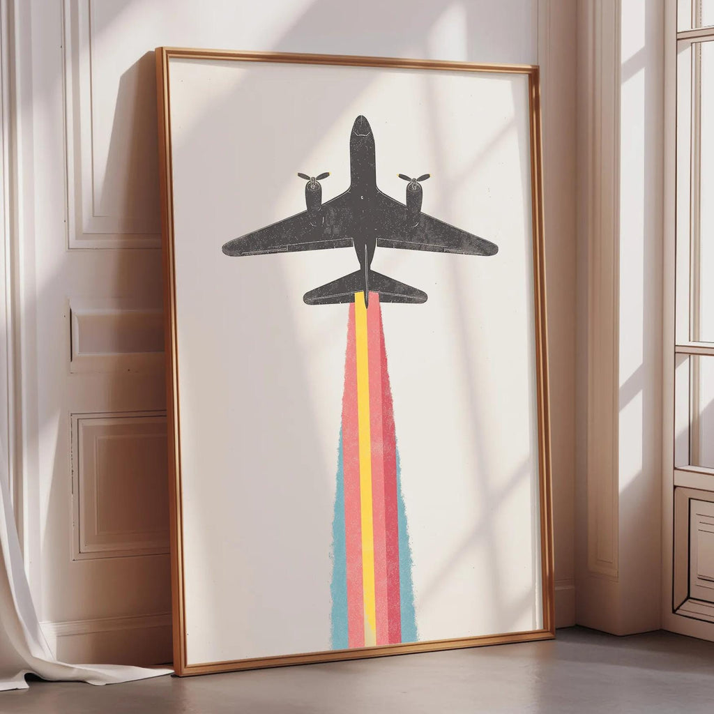 a large framed artwork depicting a plane with a colorful smoke trail, placed on a white wall near a window.