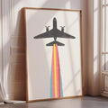 a large framed artwork depicting a plane with a colorful smoke trail, placed on a white wall near a window.