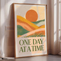 a framed poster with a vibrant, abstract landscape design and the text "ONE DAY AT A TIME" displayed prominently on it.