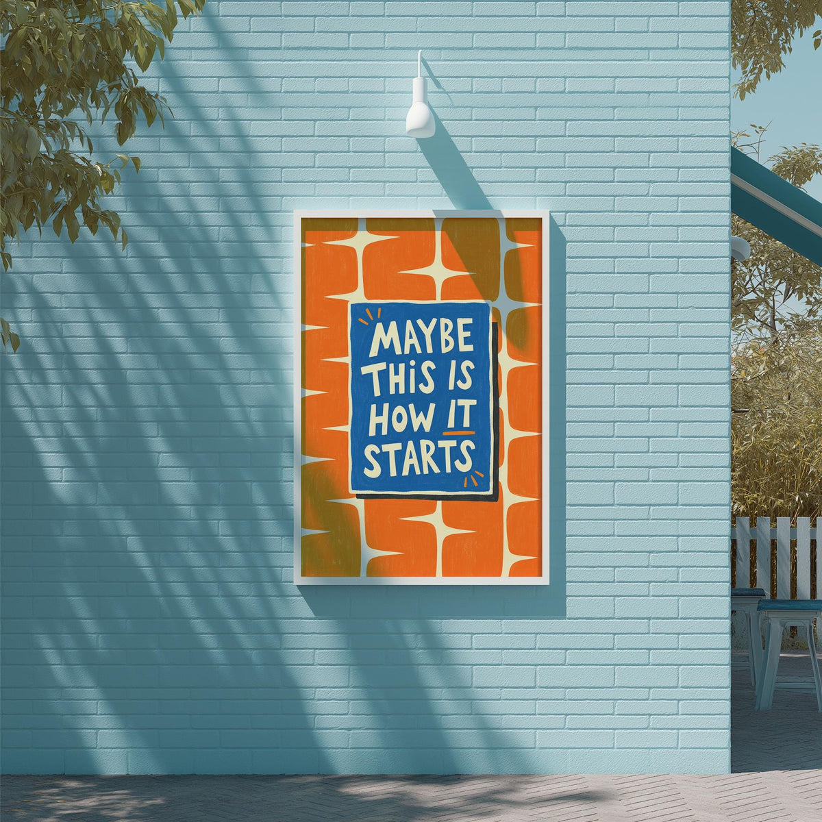a blue wall with a framed poster that reads "MAYBE THIS IS HOW IT STARTS" in white text.