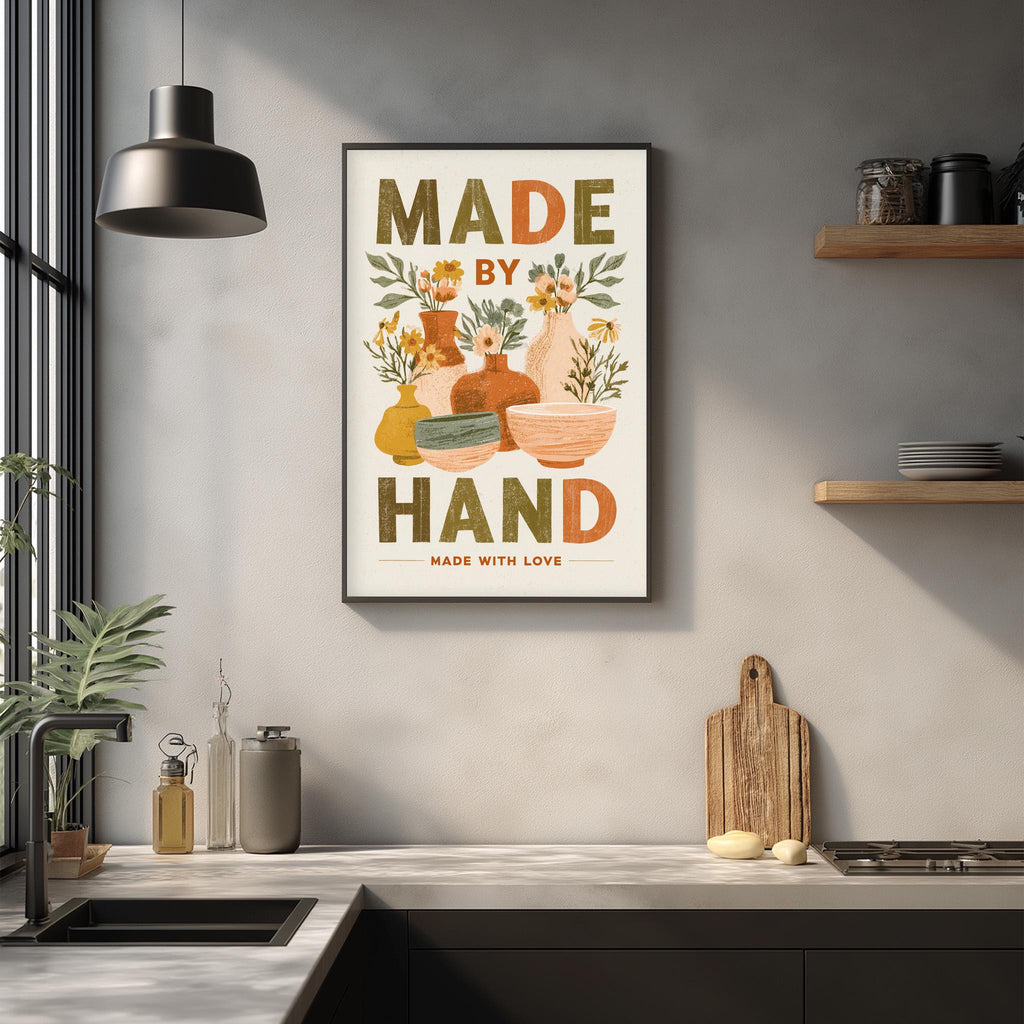 a kitchen counter with various kitchen items, such as a cutting board, a sink, and a potted plant. Above the counter, there is a framed poster with the text "MADE BY HAND MADE WITH LOVE" displayed on it.