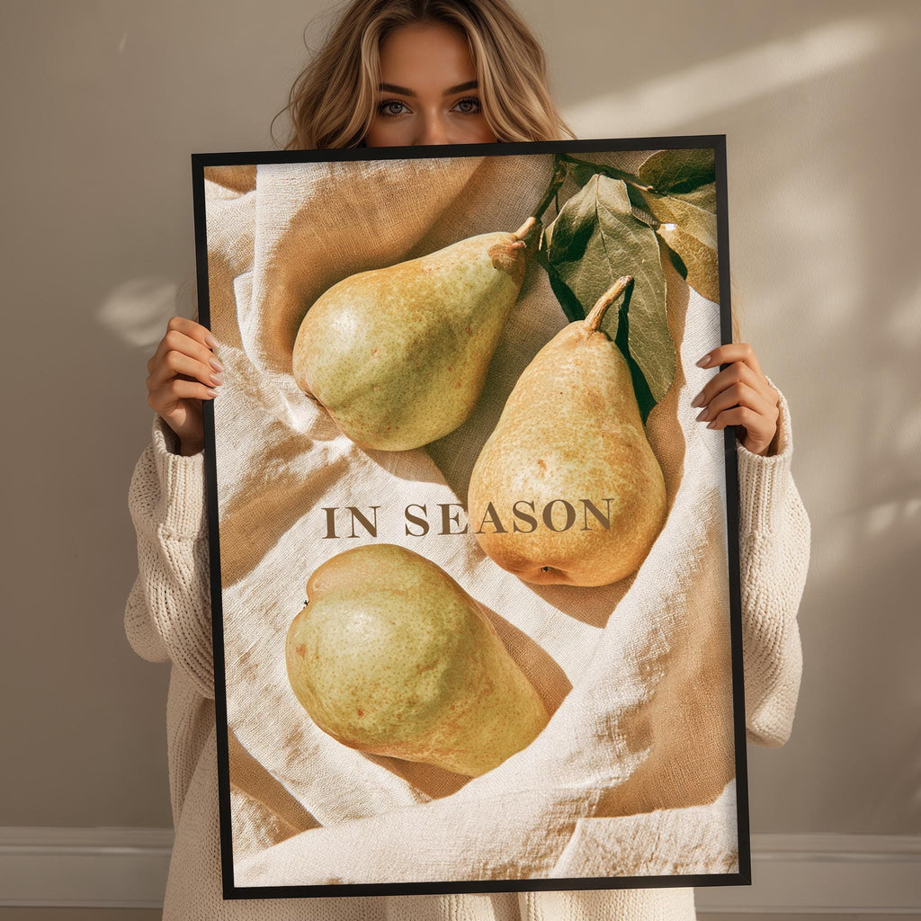 A woman holds up a framed image of pears, with the text "IN SEASON" visible on the frame.