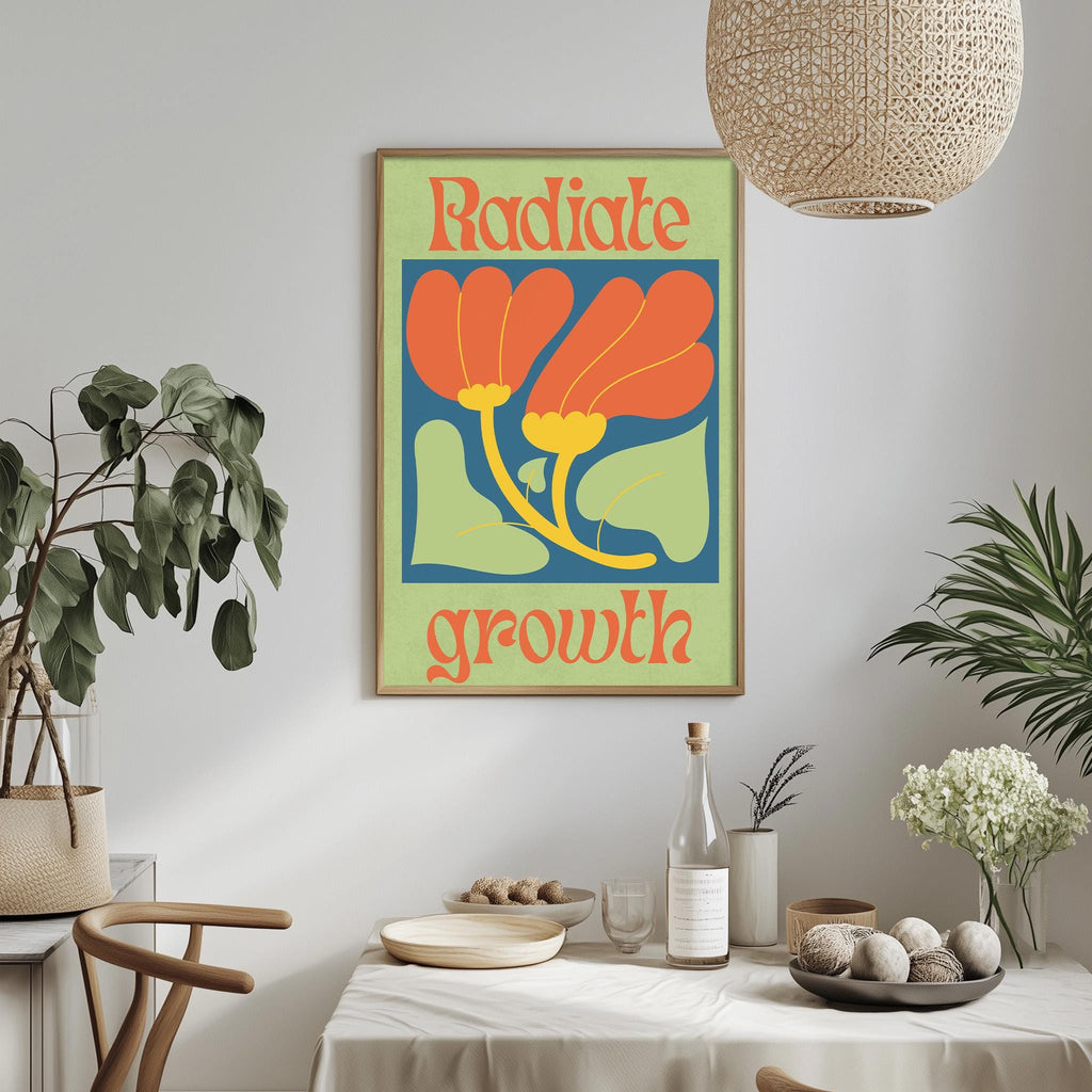 a dining table with a white tablecloth, a bowl of fruit, a bottle, and a vase with flowers. Above the table, there is a framed poster with the text "Radiate growth" in a vibrant color scheme.