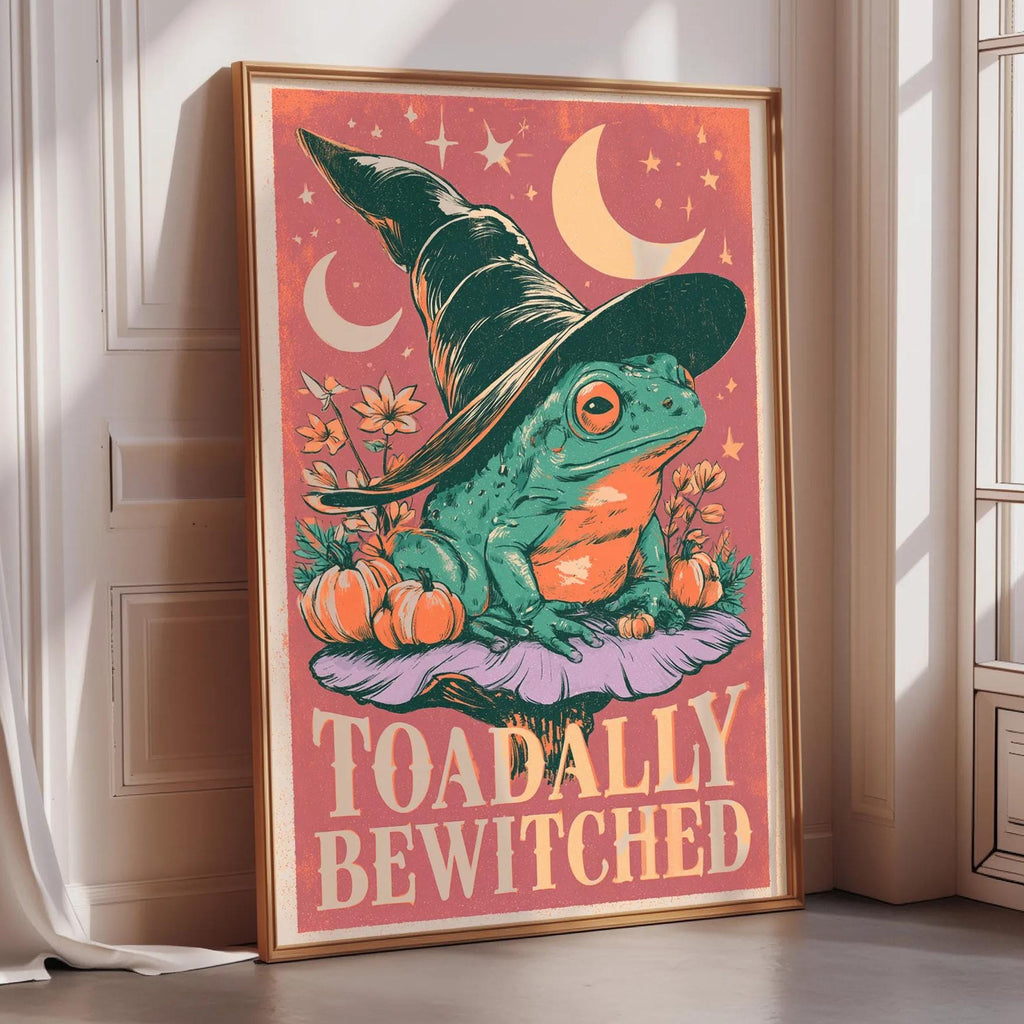 A framed poster featuring a green frog wearing a witch's hat, surrounded by pumpkins and flowers, with the text "Toadally Bewitched" displayed prominently.
