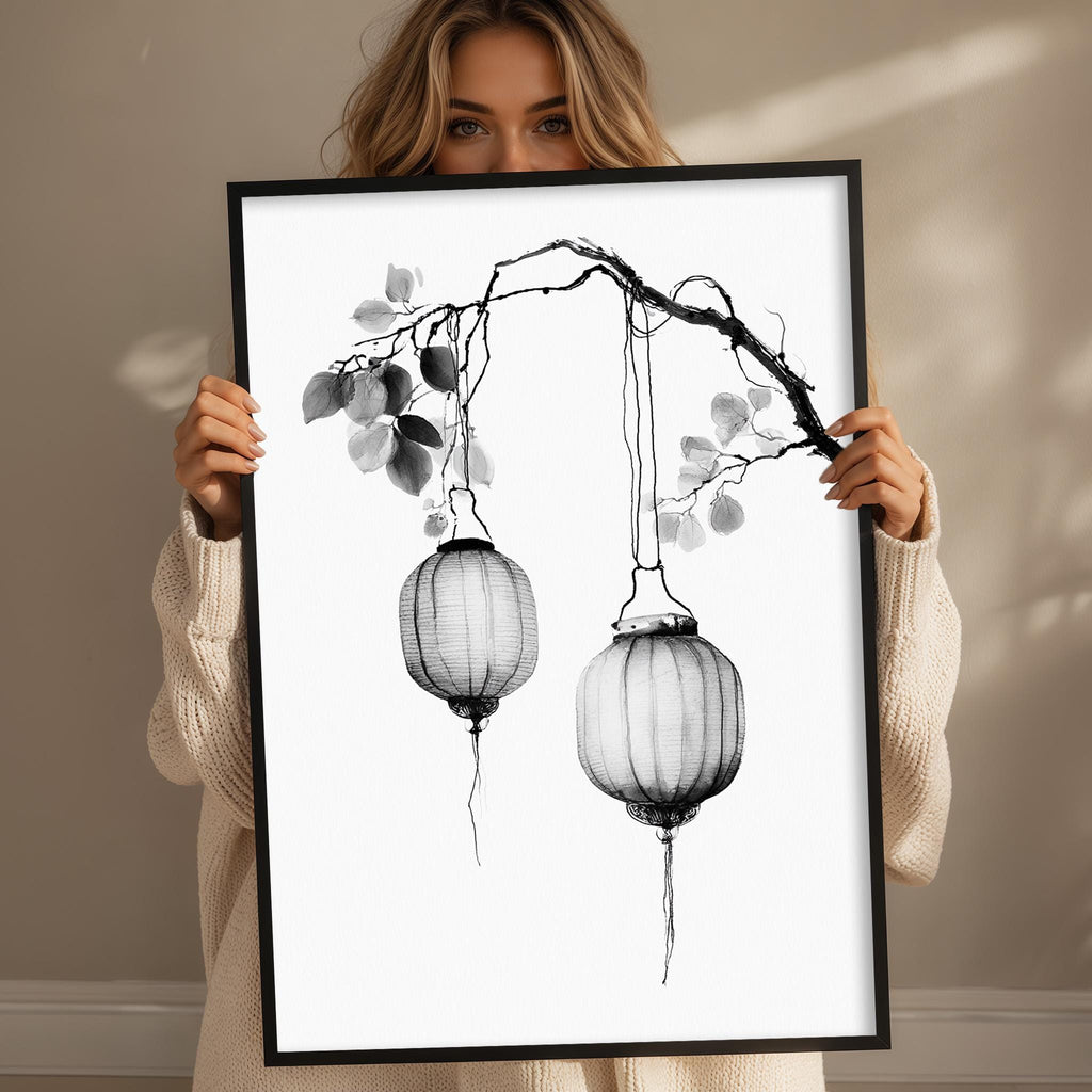 A woman holds up a framed print of two lanterns hanging from a branch.