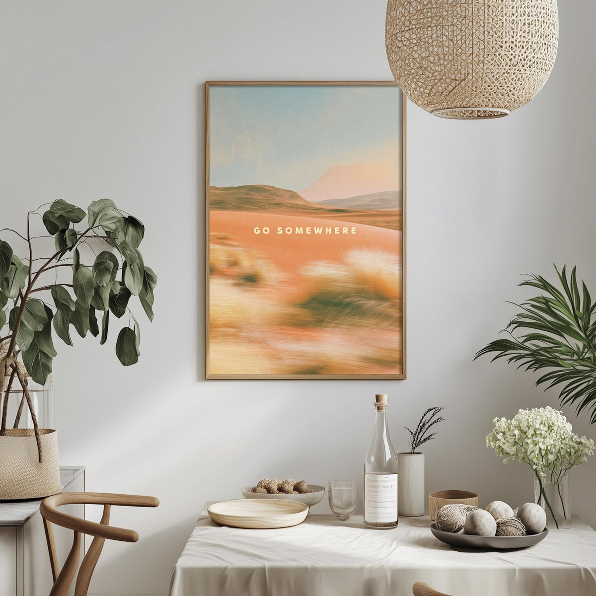 a dining table with a bowl of fruit, a bottle, and a vase of flowers, along with a framed picture hanging on the wall above the table.